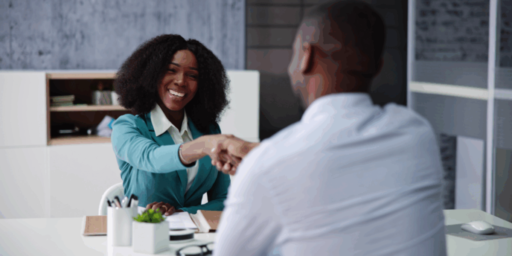 A woman is sat across from a man smiling and shaking hands.