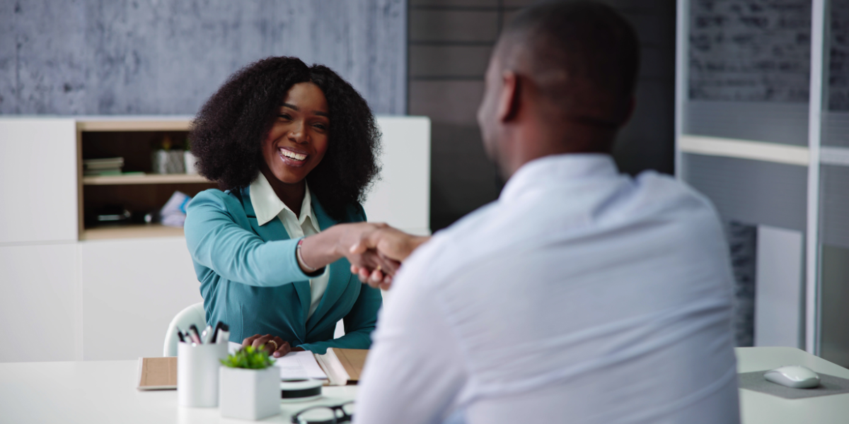 A woman is sat across from a man smiling and shaking hands.