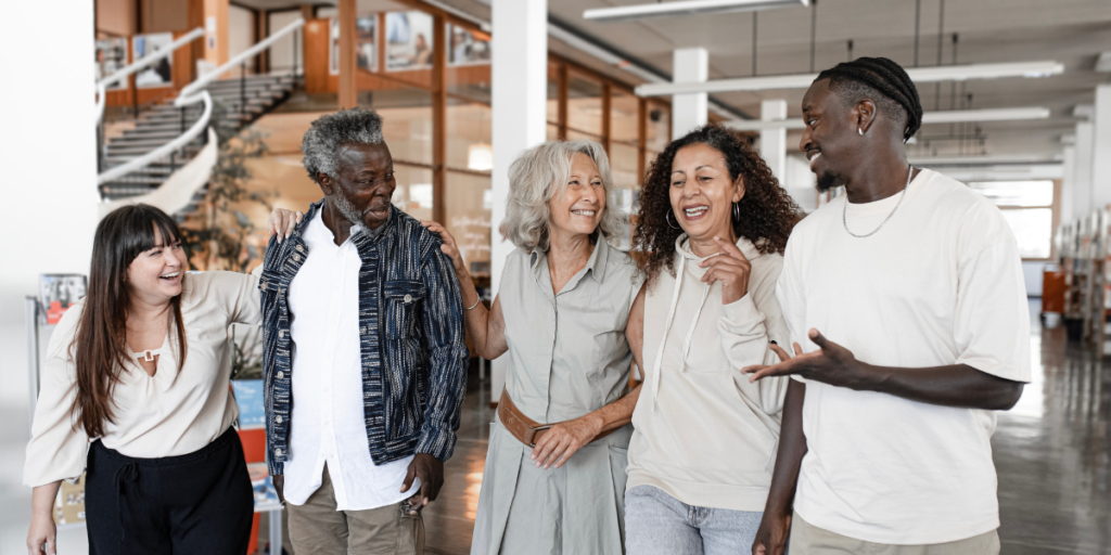 Five people are walking side-by-side chatting in an office space.