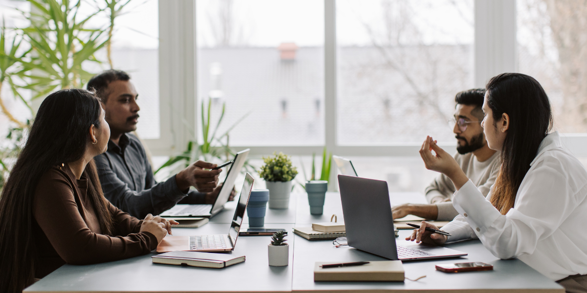Four people are sat at a boardroom table working and conversing.