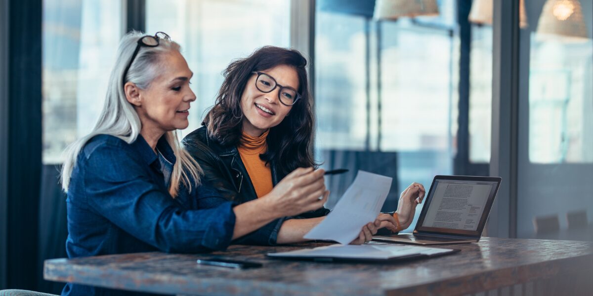 Two women are sat at a boardroom table conversing and collaborating.