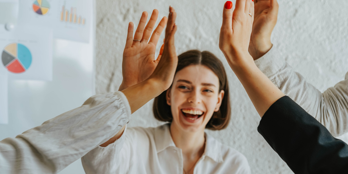A woman is smiling and raising her hand to meet those of her team members.