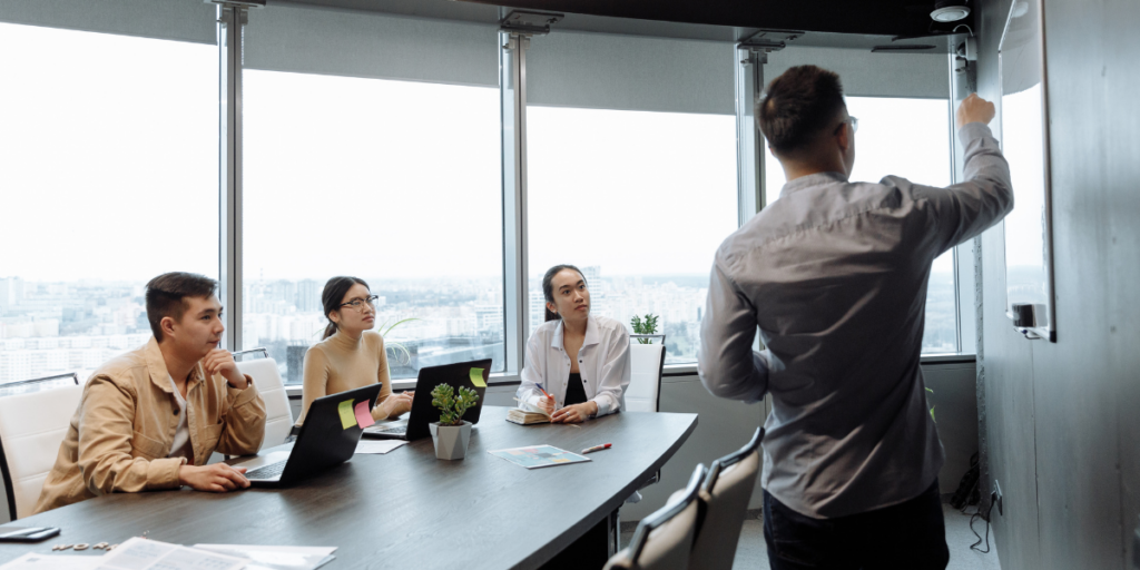 A man is stood at the front of the boardroom presenting to a group of people.