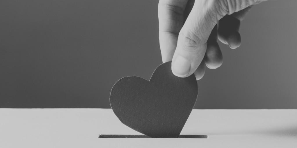 A hand is placing a paper heart in a donation box.