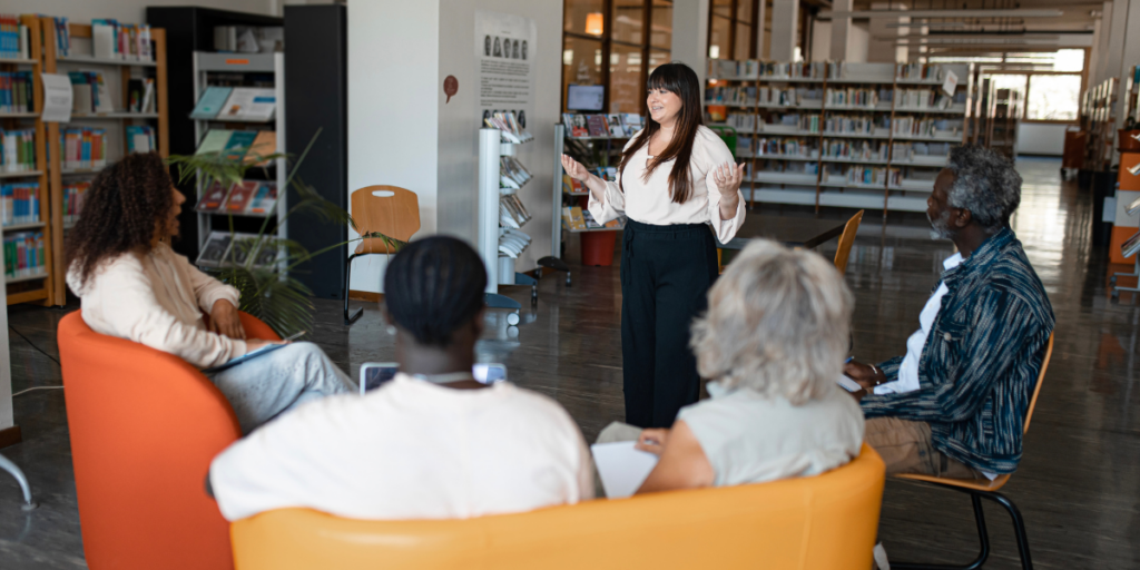 A woman is stood in front of a group of people presenting in a library.