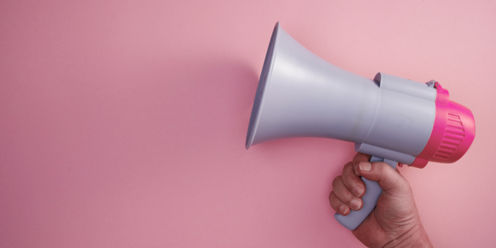 A pink megaphone held by a person. The background of the image is light pink.