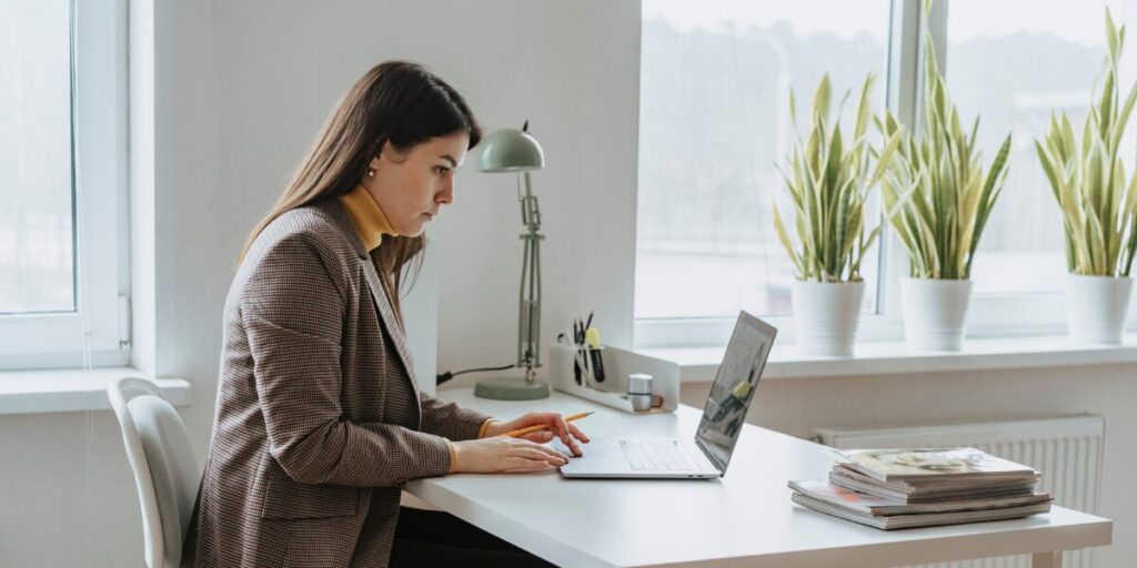 A woman is sat at her desk typing on her laptop.