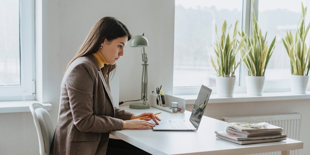 A woman is sat at her desk typing on her laptop.