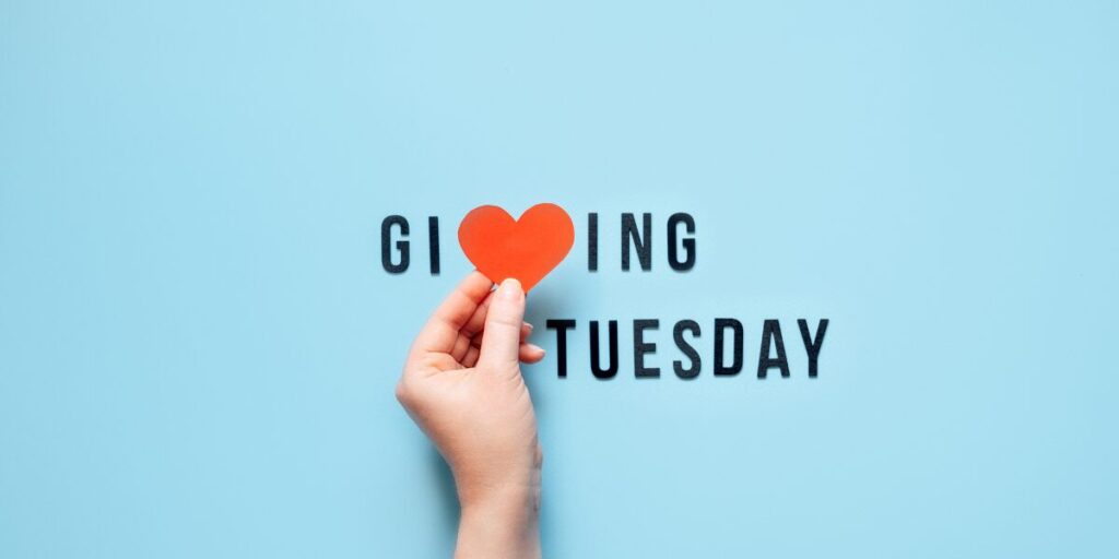 GivingTuesday with a heart representing the "v" in the text line. With a blue background and hand holding the heart.