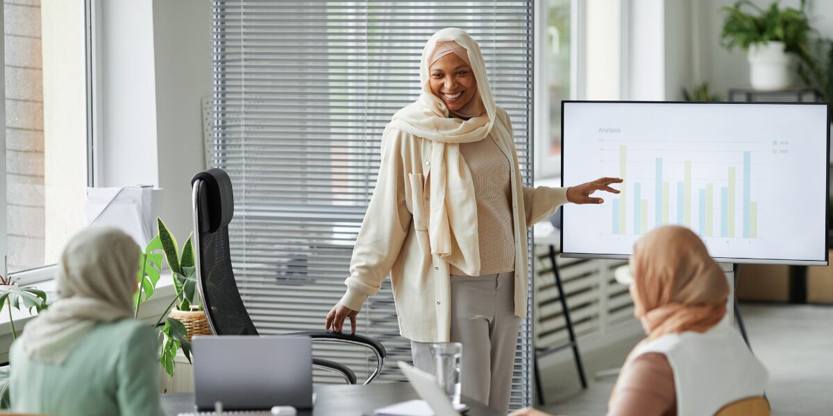 A woman is stood at the front of a boardroom presenting.