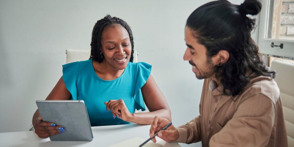 A woman is sat next to a person working on a project.