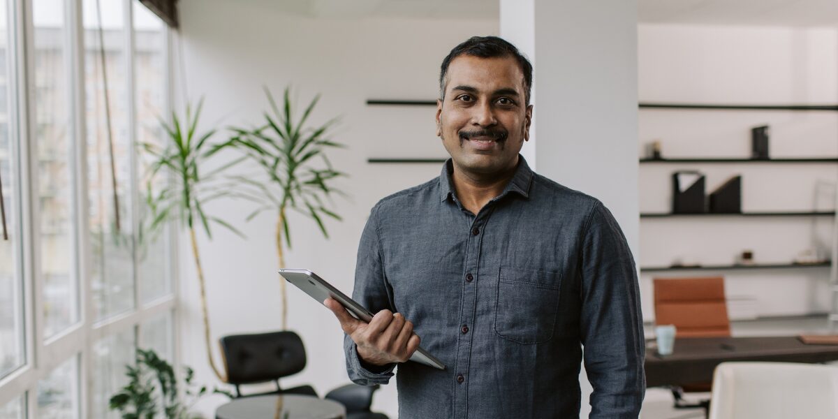 A man is stood smiling and facing the camera holding a tablet.