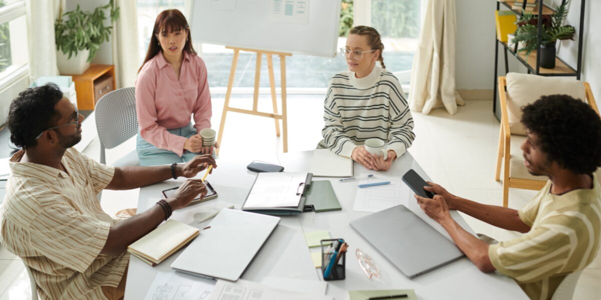 Four people are sat at a boardroom table working.