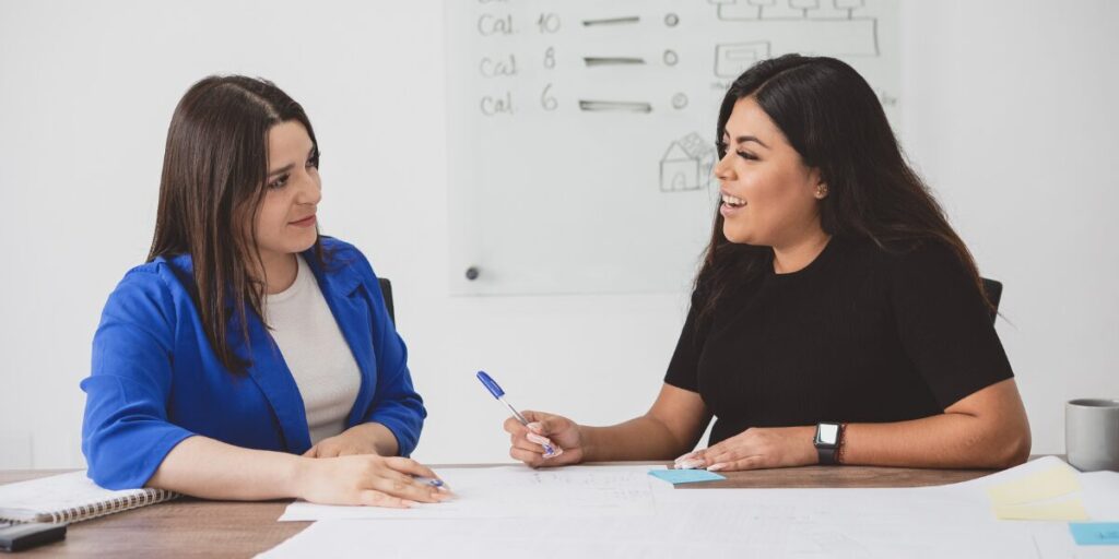 Two women are sat next to one another working together.