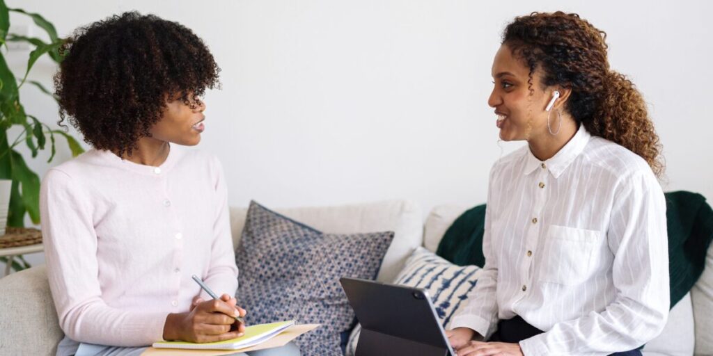 Two women are sat next to one another working in an office space.