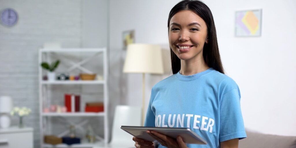 A woman is stood wearing a blue volunteer shirt holding a tablet.