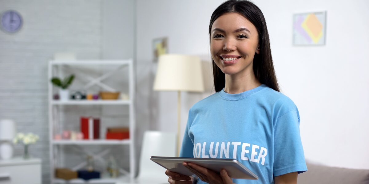 A woman is stood wearing a blue volunteer shirt holding a tablet.