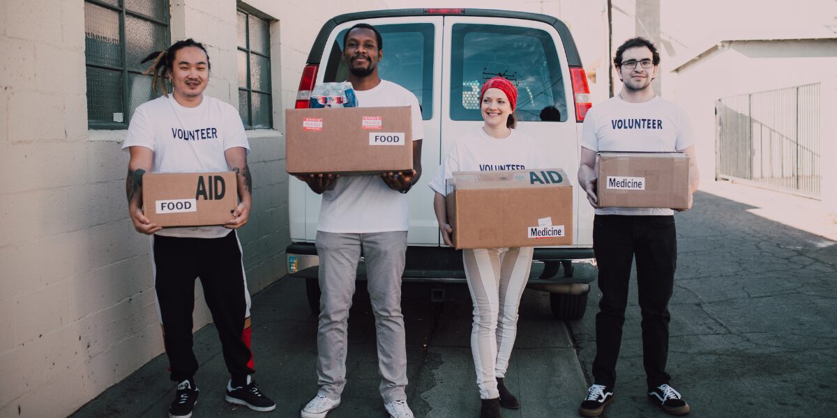 Four people volunteering are stood outside in front of a white van holding donation boxes.
