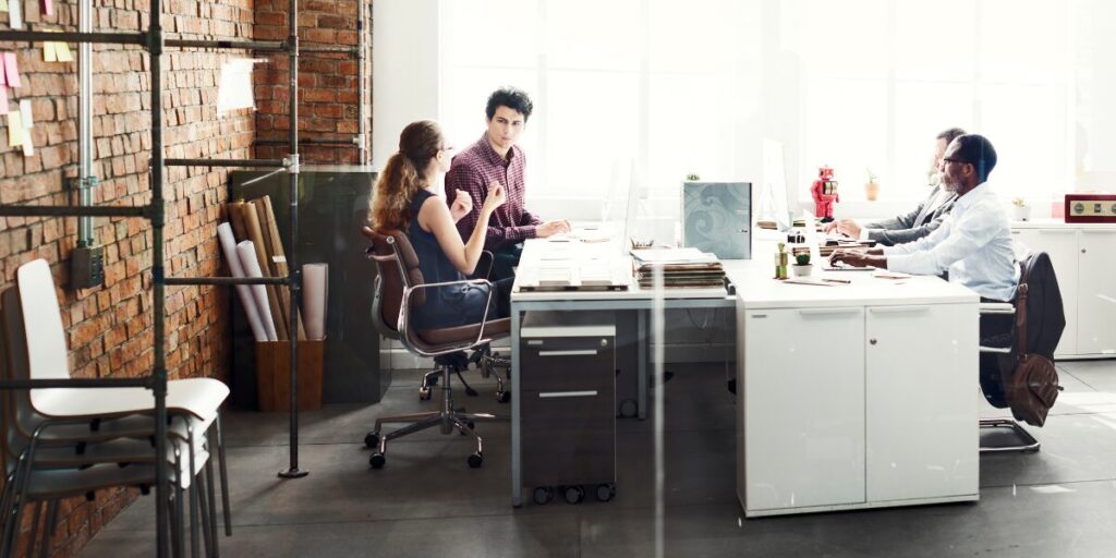 A group of four people are working in an office space and conversing.