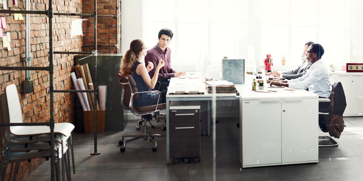 A group of four people are working in an office space and conversing.