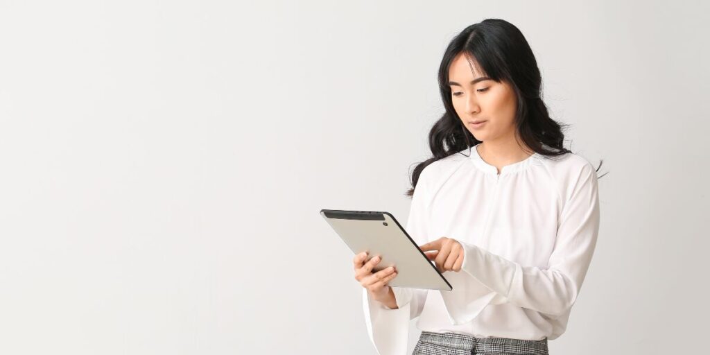 A woman is stood holding a tablet and appearing to work.