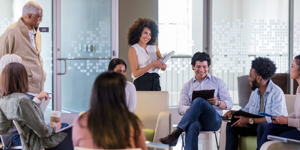 A group of people are meeting in an office space conversing and working.
