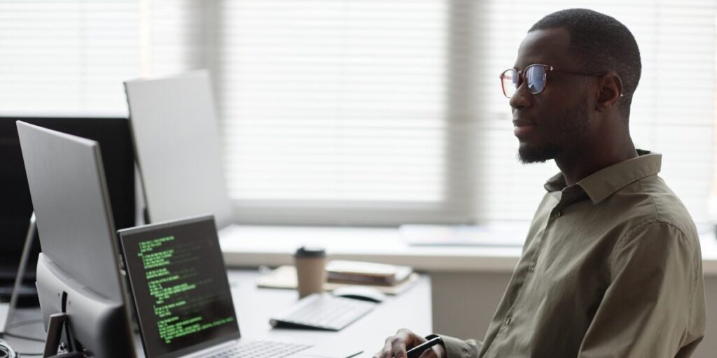 A man is sat at his laptop working on a code piece.