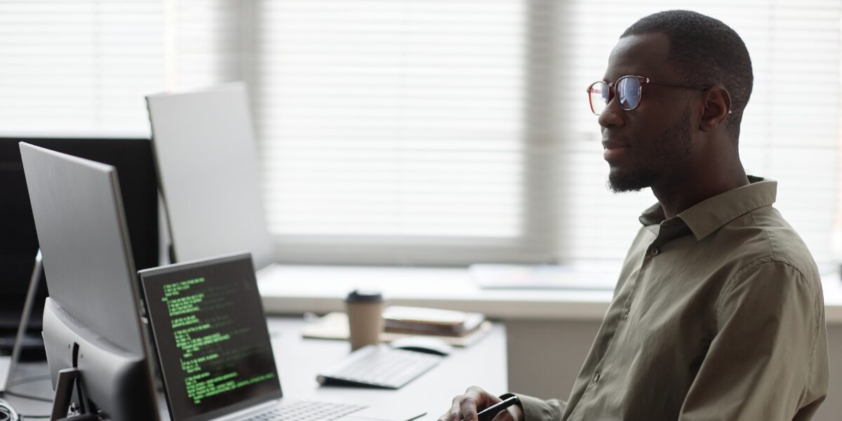 A man is sat at his laptop working on a code piece.