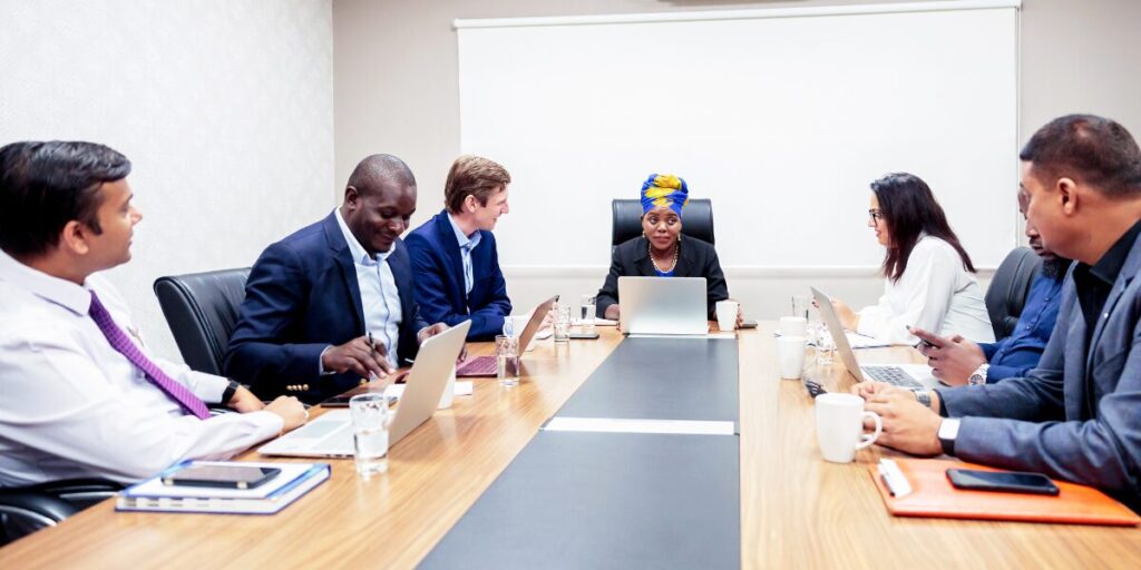 Board meeting with seven people sitting at a boardroom table conversing.