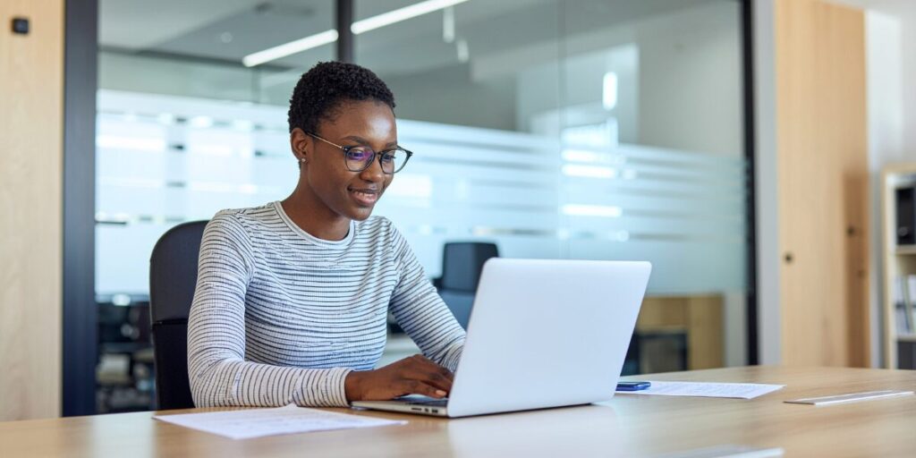 A woman is sat at a boardroom table working on a laptop.