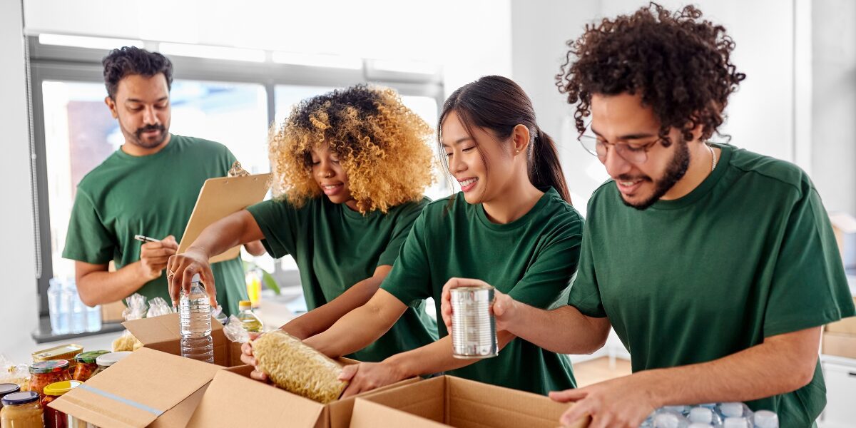 Four people are volunteering at a food bank and are packaging boxes of food.