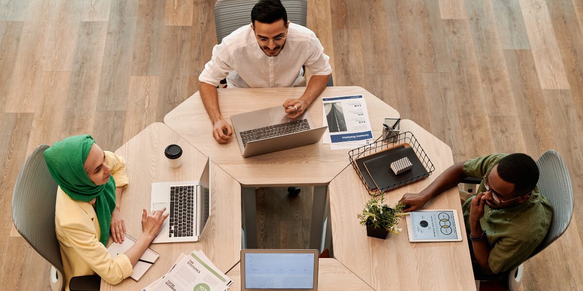 Three people are sat at a boardroom table working and conversing.