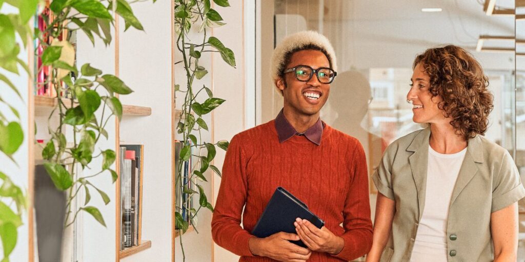 Two people are walking side-by-side in an office space and conversing.
