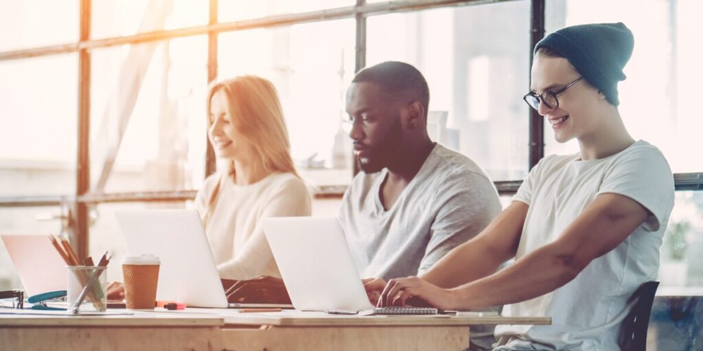 Three people are sat in an open office space working on their laptops.