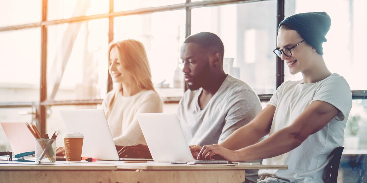 Three people are sat in an open office space working on their laptops.