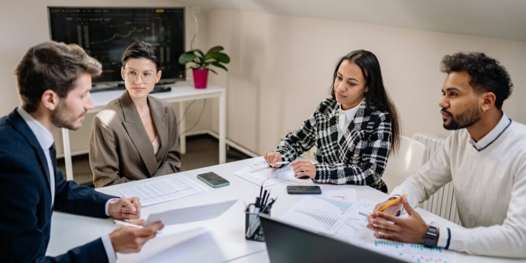 Four people are sat in an office space working and conversing.
