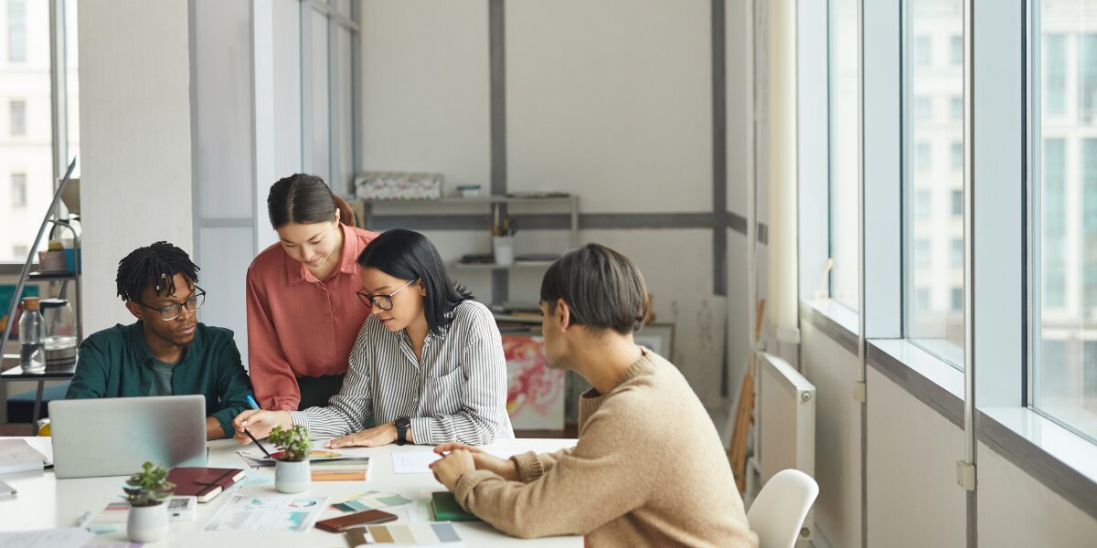 Four people are gathered around a boardroom table reviewing documentation.