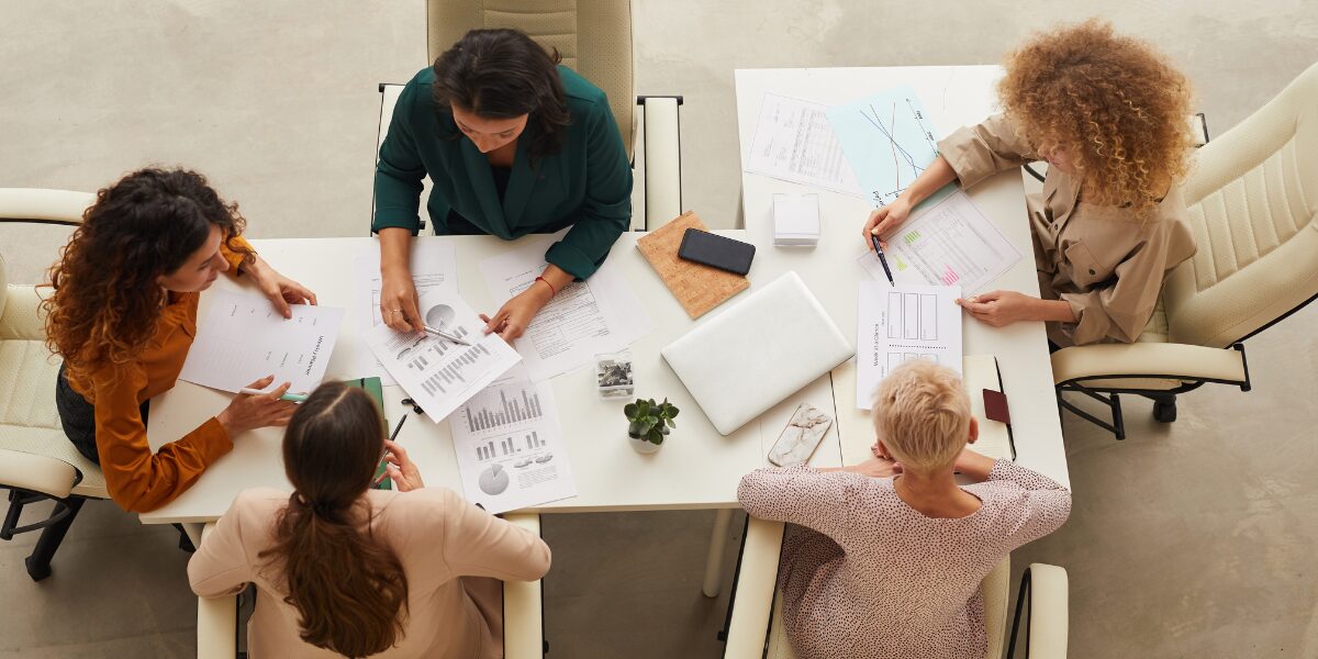 A group of people are sat in a board room working and conversing.