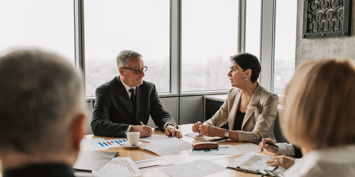 A group of people are sat in a board room working and conversing.