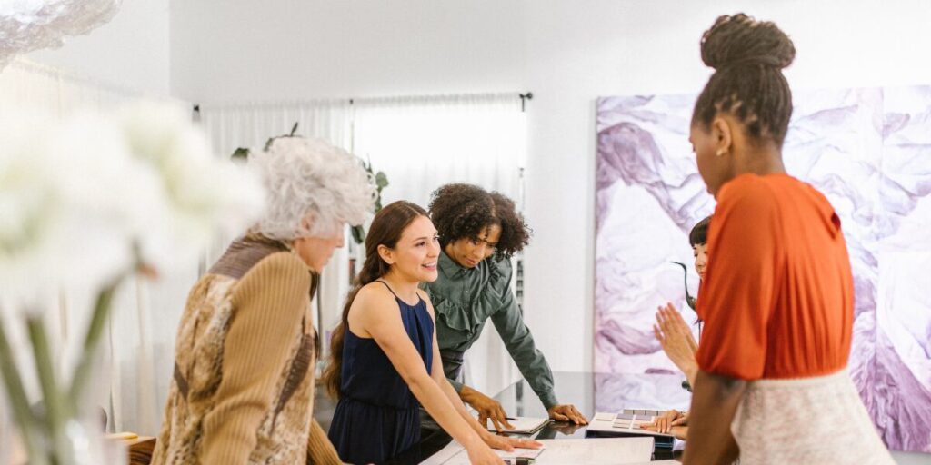 A group of people are stood around a boardroom table working and conversing.