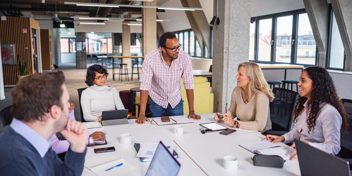 A group of people are meeting in a boardroom conversing and working.