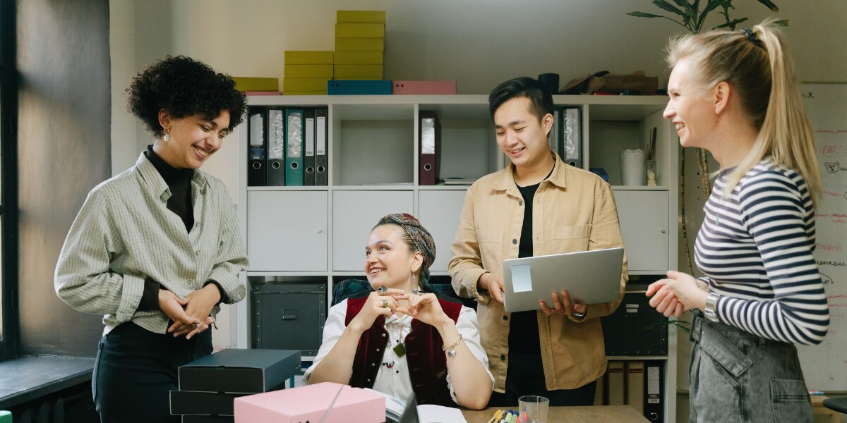 Four people are gathered around a boardroom table in an office space conversing and working.