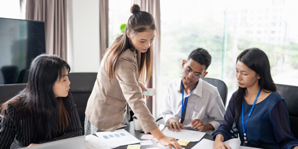 Four people are gathered around a boardroom table conversing and working.